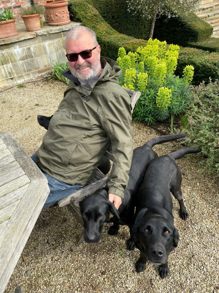Picture of David O'Hara sitting outside with three black labrador dogs